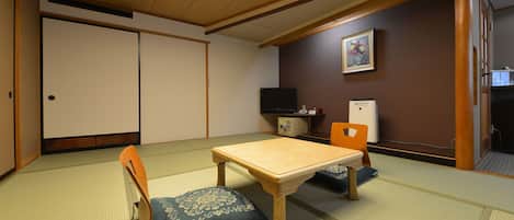 A traditional Japanese-style room with tatami flooring, a low wooden table, and a television on a stand.