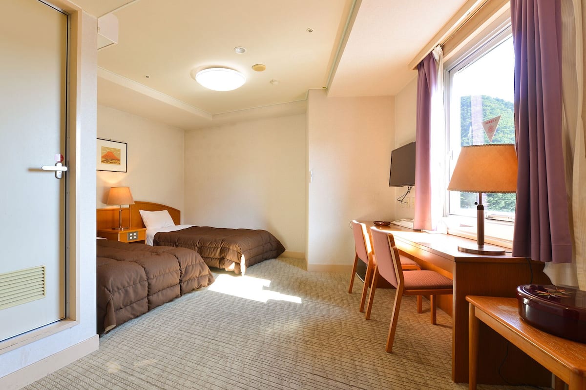 Ett hotellrum med en säng, ett skrivbord med en stol, en tv och ett fönster med gardiner.