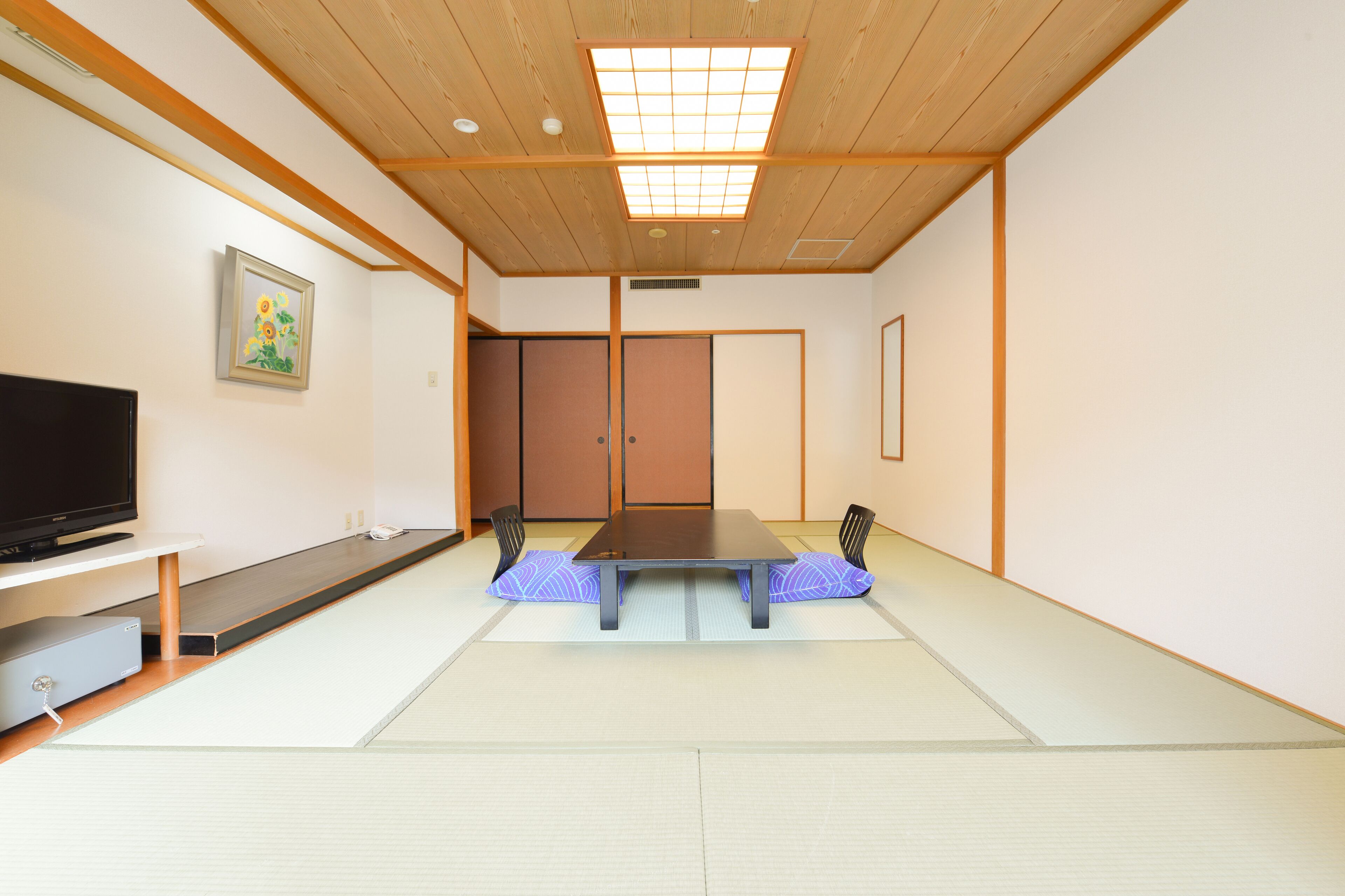 A traditional Japanese room with tatami flooring, a low table, and a television on a stand.
