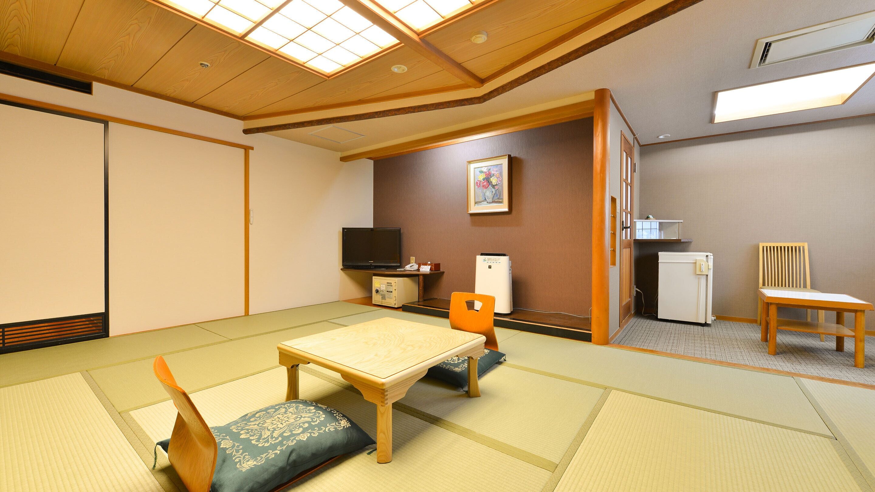 Um quarto em estilo japonês tradicional, com tatames, uma mesa baixa, uma cadeira acolchoada, uma televisão, um frigorífico e um micro-ondas.
