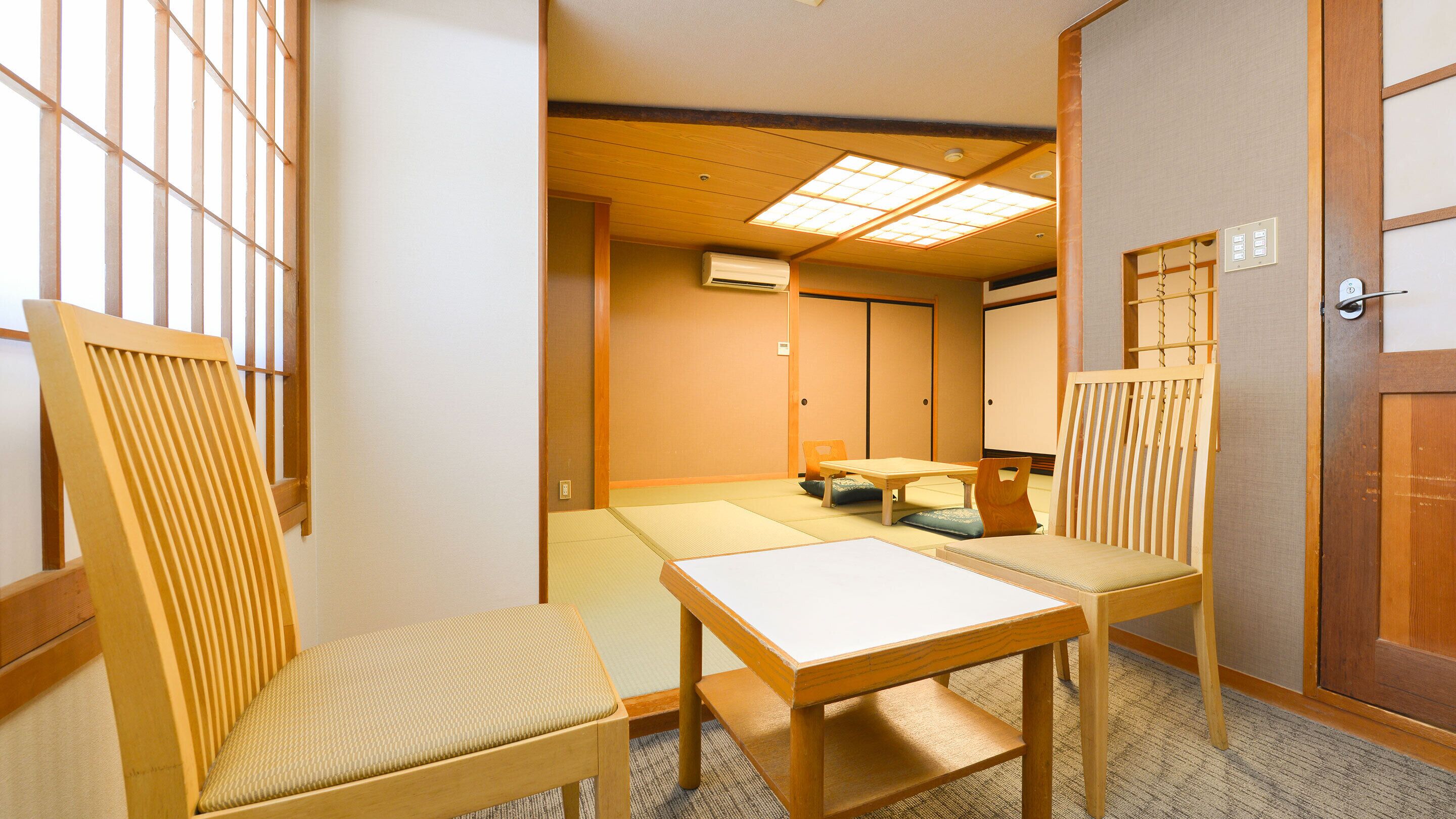 A traditional Japanese room with tatami mats, a low wooden table, and two tatami chairs.