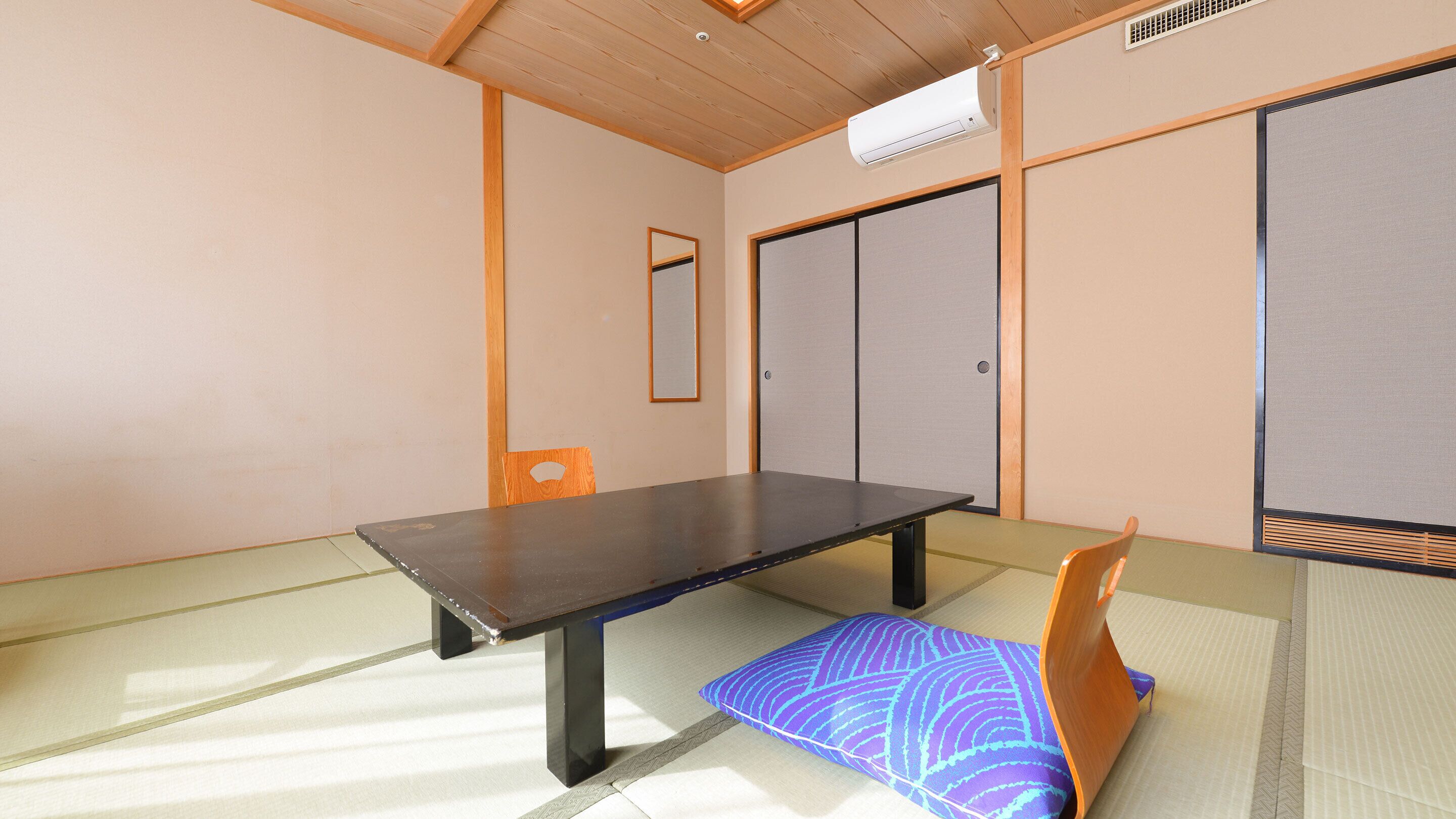 A traditional Japanese room with tatami flooring, a low table, a cushion, sliding doors, and a ceiling vent.