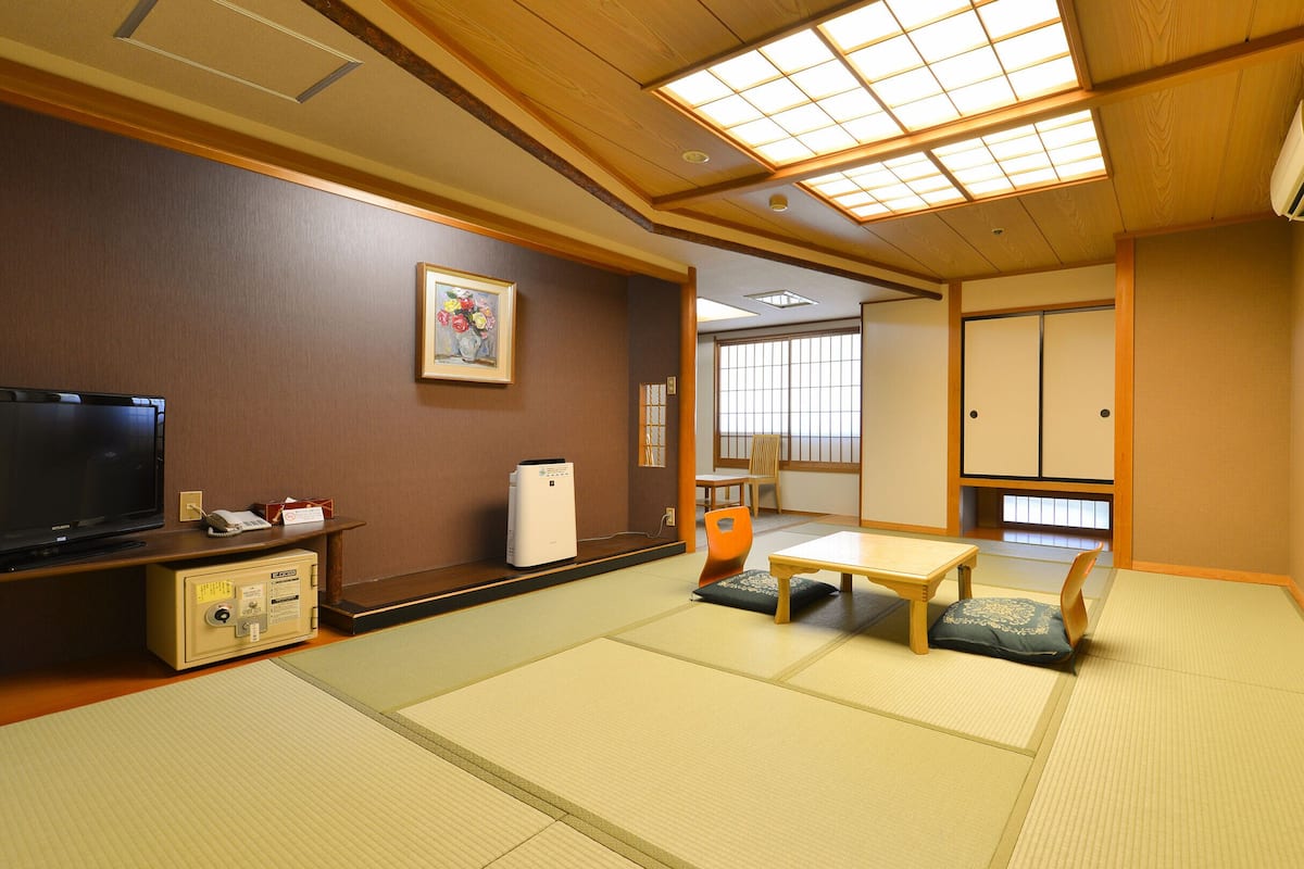 Ett traditionellt japanskt rum med tatamimattor på golvet, en tv, en värmare och en skjutdörr.