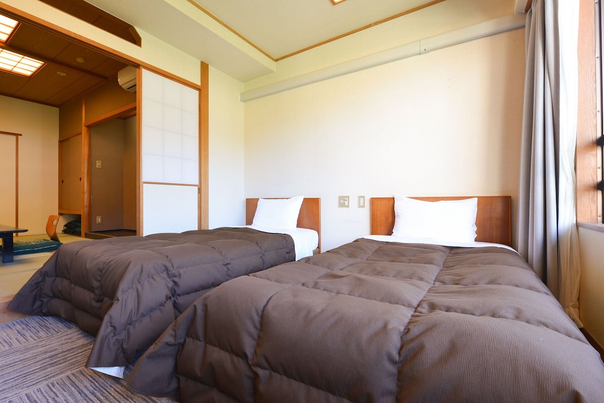 Ett hotellrum med två sängar, en sänggavel i trä, en tatamimatta och en traditionell japansk skjutdörr.