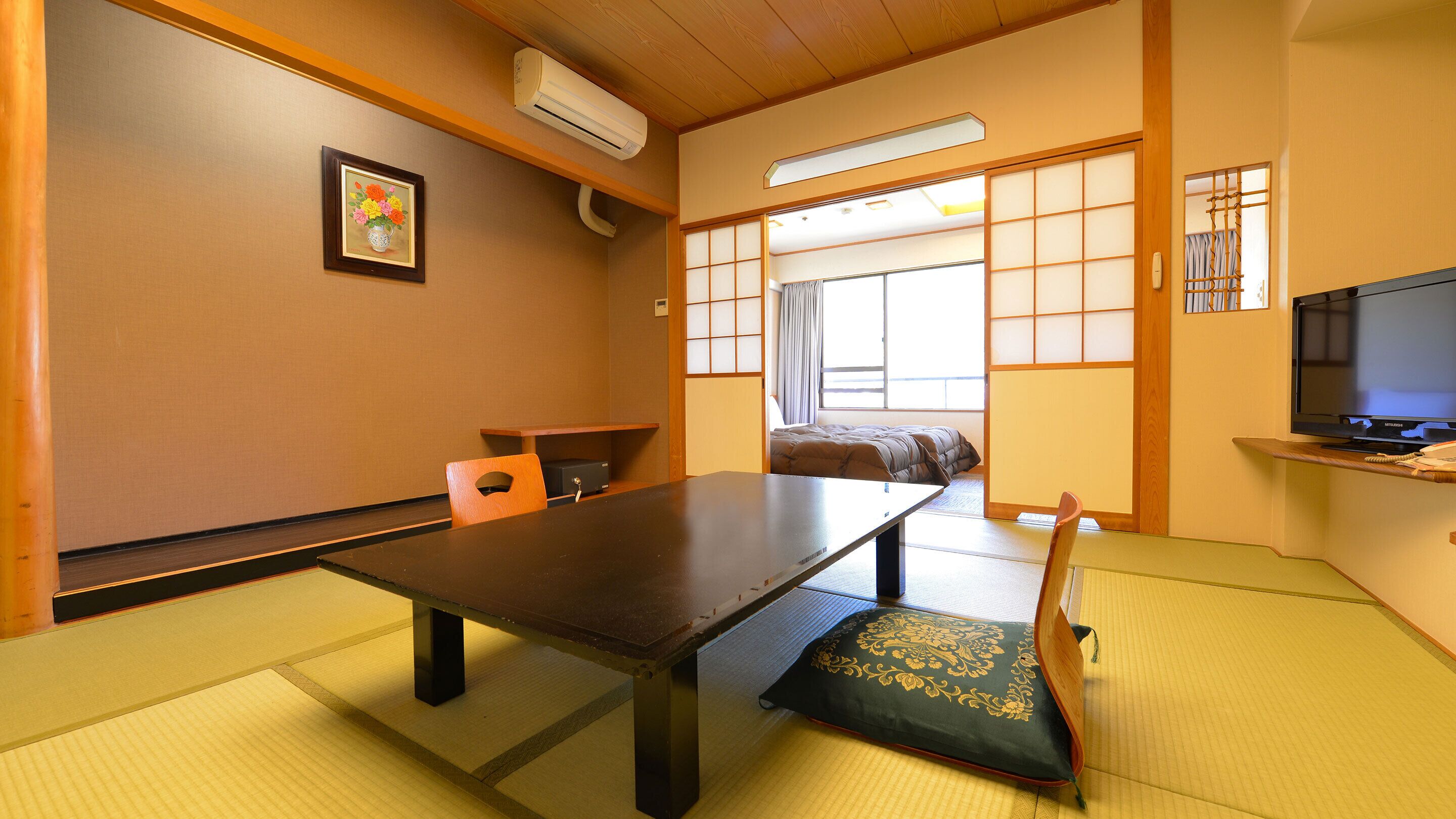 A traditional Japanese room with tatami flooring, a low table, a sofa, and a television.