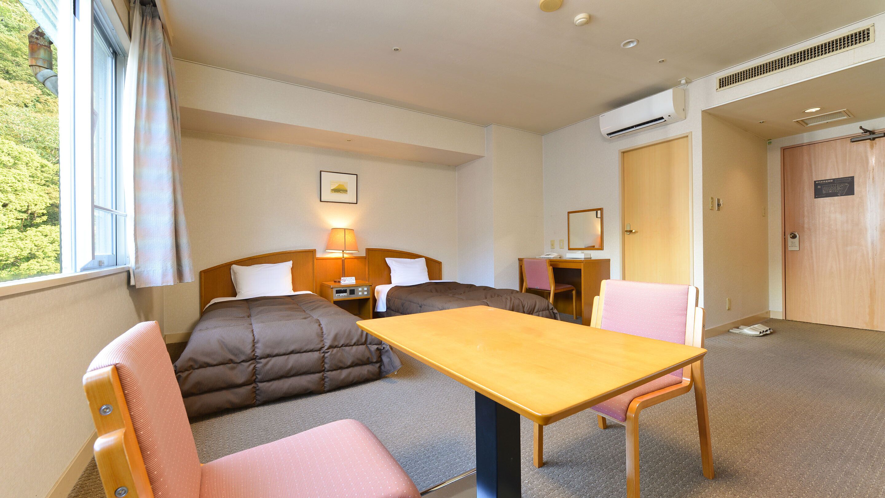 A hotel room with a bed, a desk, a chair, a table, and a window with curtains.
