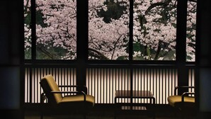 A room with a large window displaying cherry blossoms, two chairs, and a small table.