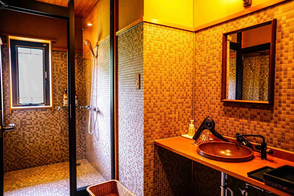 Ein Badezimmer mit gefliestem Duschbereich, einem Waschbecken mit Spiegel und einem Fenster.
