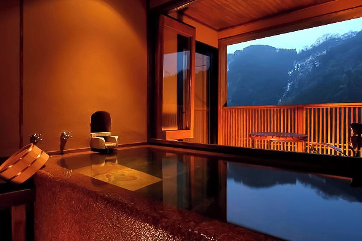 Ein Zimmer mit einem in Glas eingefassten Pool, einer Holzterrasse und Blick auf die Berge.