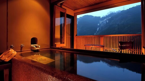 A room with a glass-enclosed pool, wooden deck, and a view of mountains.