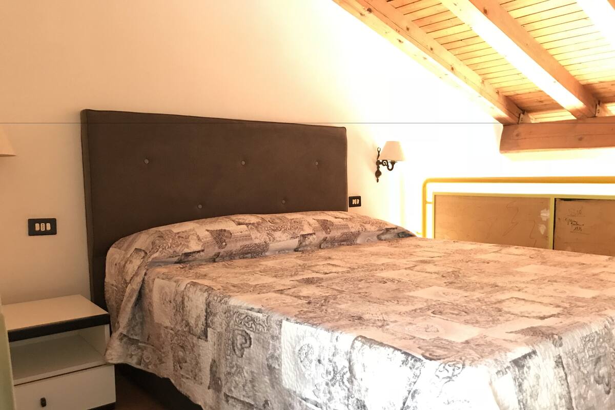 A bedroom with a bed, nightstand, and a wall-mounted lamp.