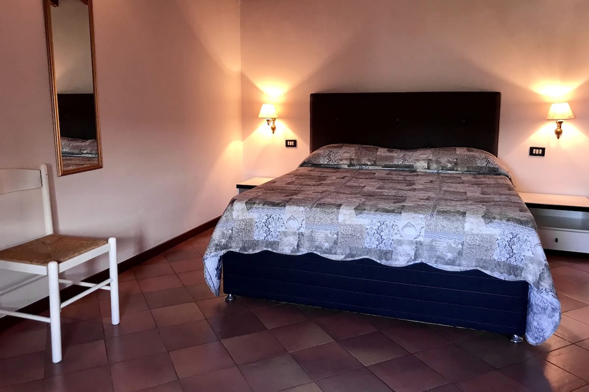 A bedroom with a bed, two bedside lamps, a chair, and a mirror.