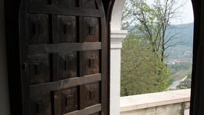 A wooden door with a metal handle, leading to a balcony with a view of a landscape and a distant town. - Ca' Pignoi (Garda)