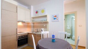 A compact kitchen with modern appliances, a dining area with a table and chairs, and a shower visible through an open door. - Sarap apartments Budva (Budva)