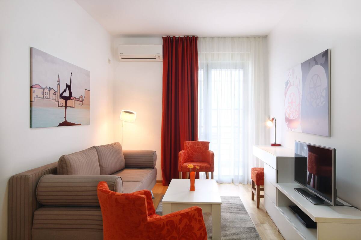 Una sala de estar moderna con un sofá, dos sillones, una mesa de centro, un televisor y obras de arte en las paredes.