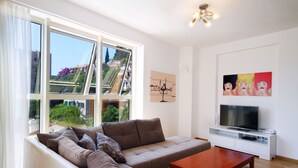 A modern living room with a sofa, a coffee table, a TV on a white stand, and artwork on the walls. - Sarap apartments Budva (Budva)