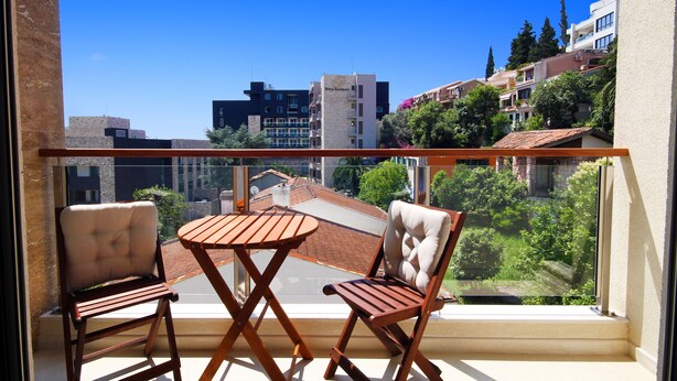 A balcony with two wooden chairs and a small table, overlooking a cityscape with buildings and greenery. - Sarap apartments Budva (Budva)