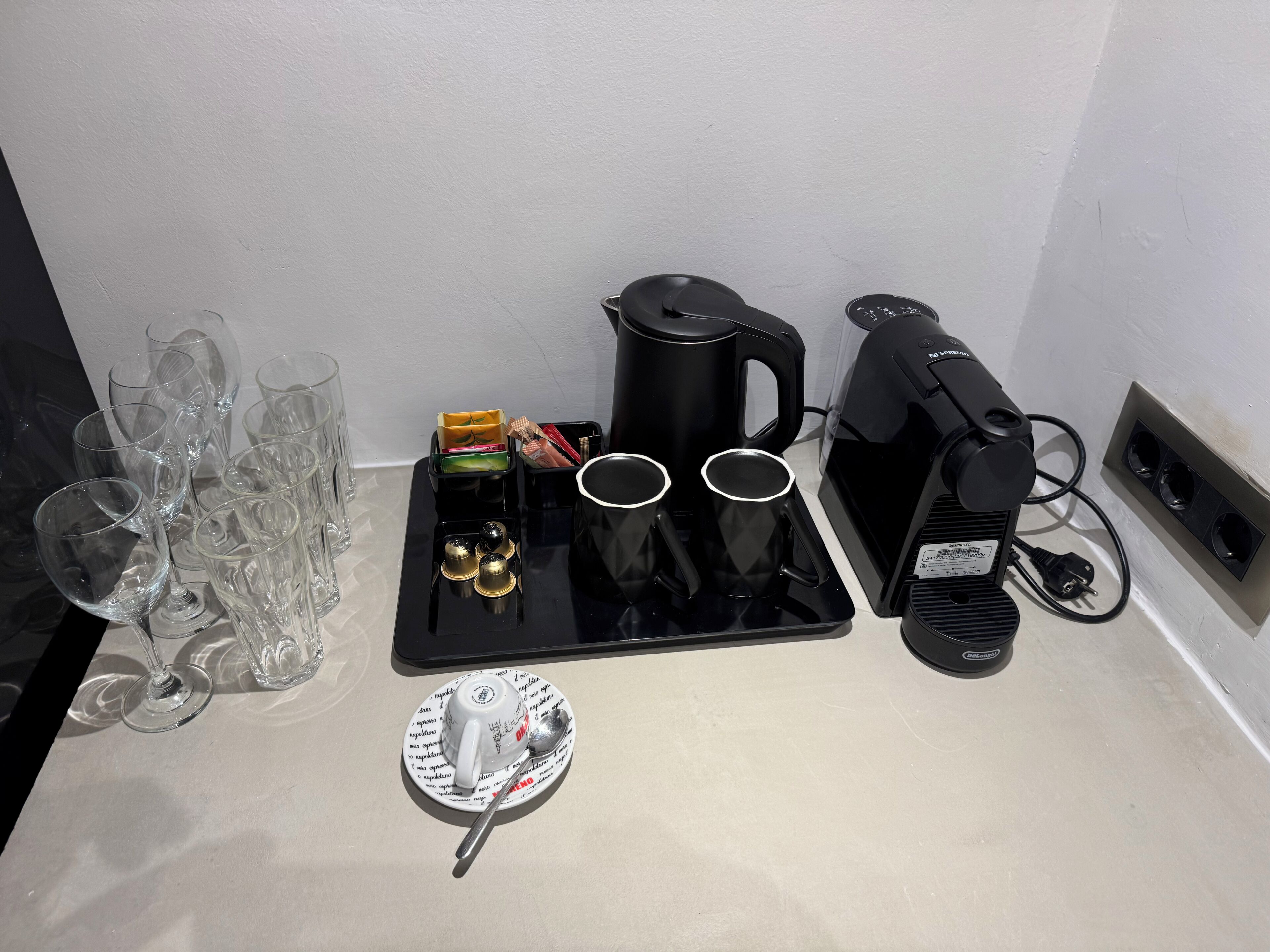 En kaffestation med kaffemaskine, kopper og en tallerken med ske.