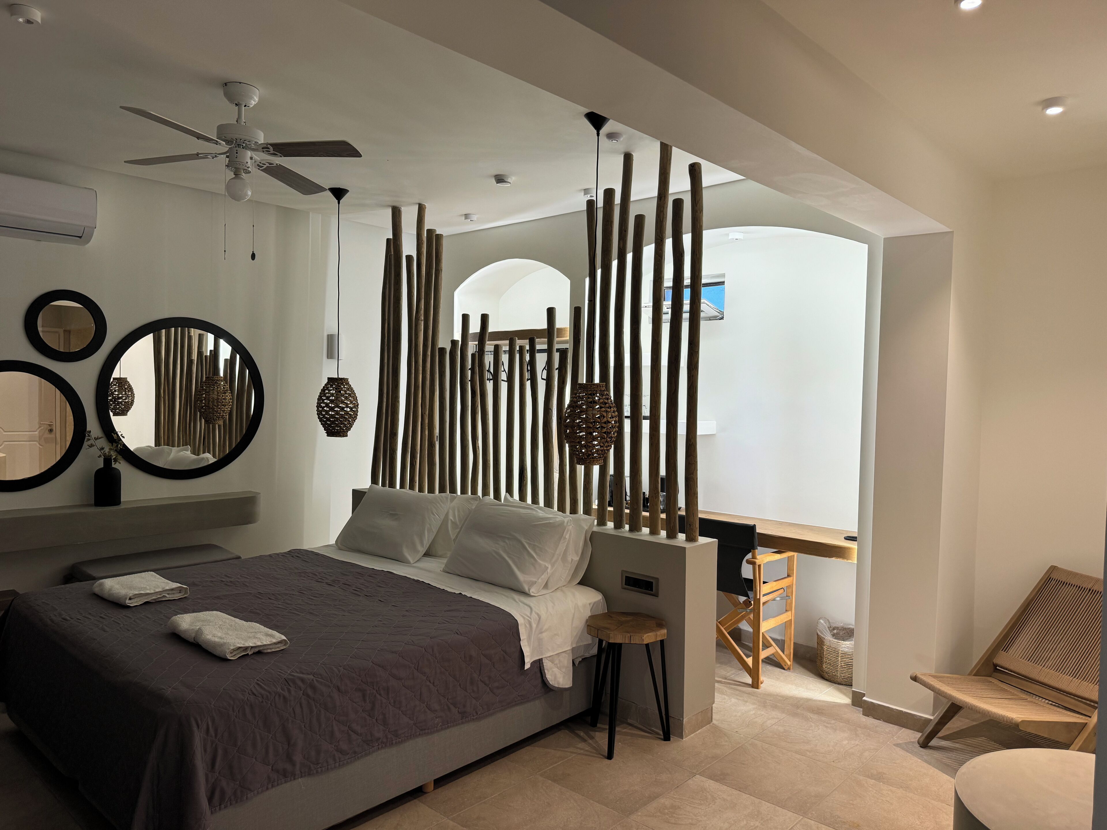 A modern bedroom with a bed, bedside tables, a ceiling fan, and a decorative wooden partition.