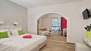A hotel room with a large bed, a desk, and a view of the sea through an arched doorway. - CHC Sound of the Sea (Karpathos)