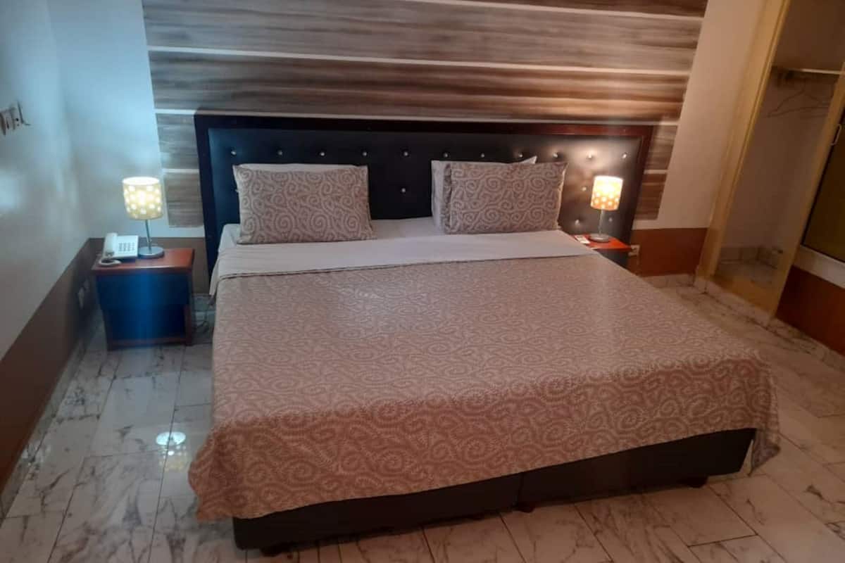 Ein Hotelzimmer mit einem großen Bett, zwei Nachttischlampen, einem Holz-Kopfteil und einem Marmorboden.