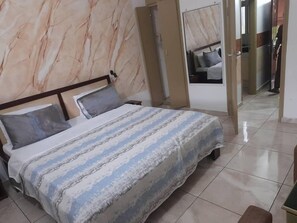 A hotel room with a bed, a nightstand, a mirror, and a wardrobe. -  Résidence Hôtel Carmel (Cocody) (Abidjan)