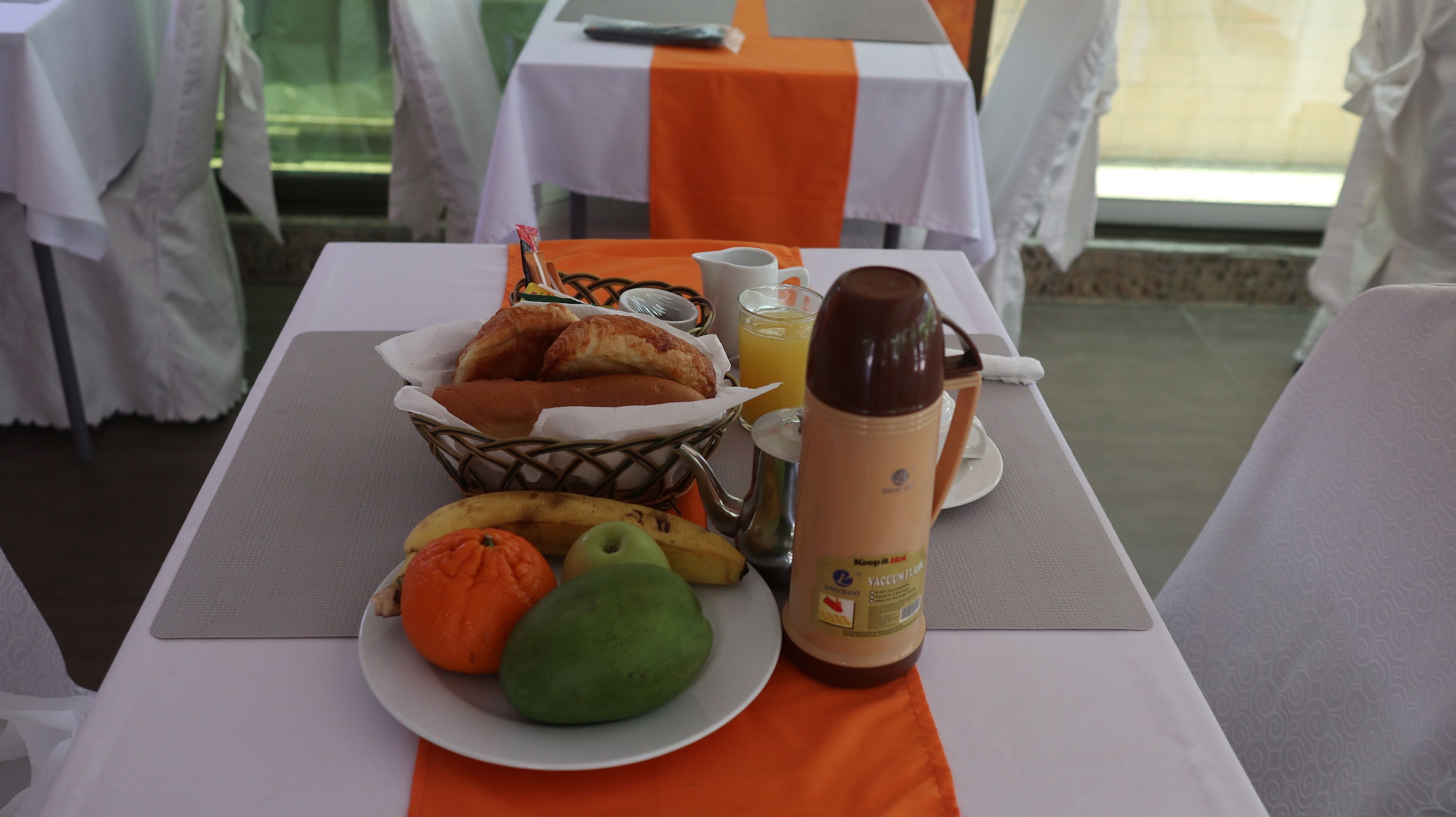 Une table de petit-déjeuner avec des croissants, des fruits, une cafetière et un verre de jus.