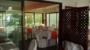 A dining area with tables set for guests, large windows, and a view of the outdoors.