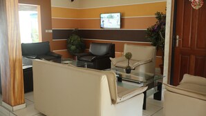 A modern waiting area with leather sofas, a glass coffee table, and a television mounted on the wall.