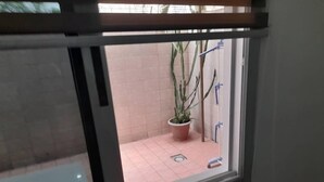 A window view of a tiled patio area with a potted plant and a blue object on the floor.