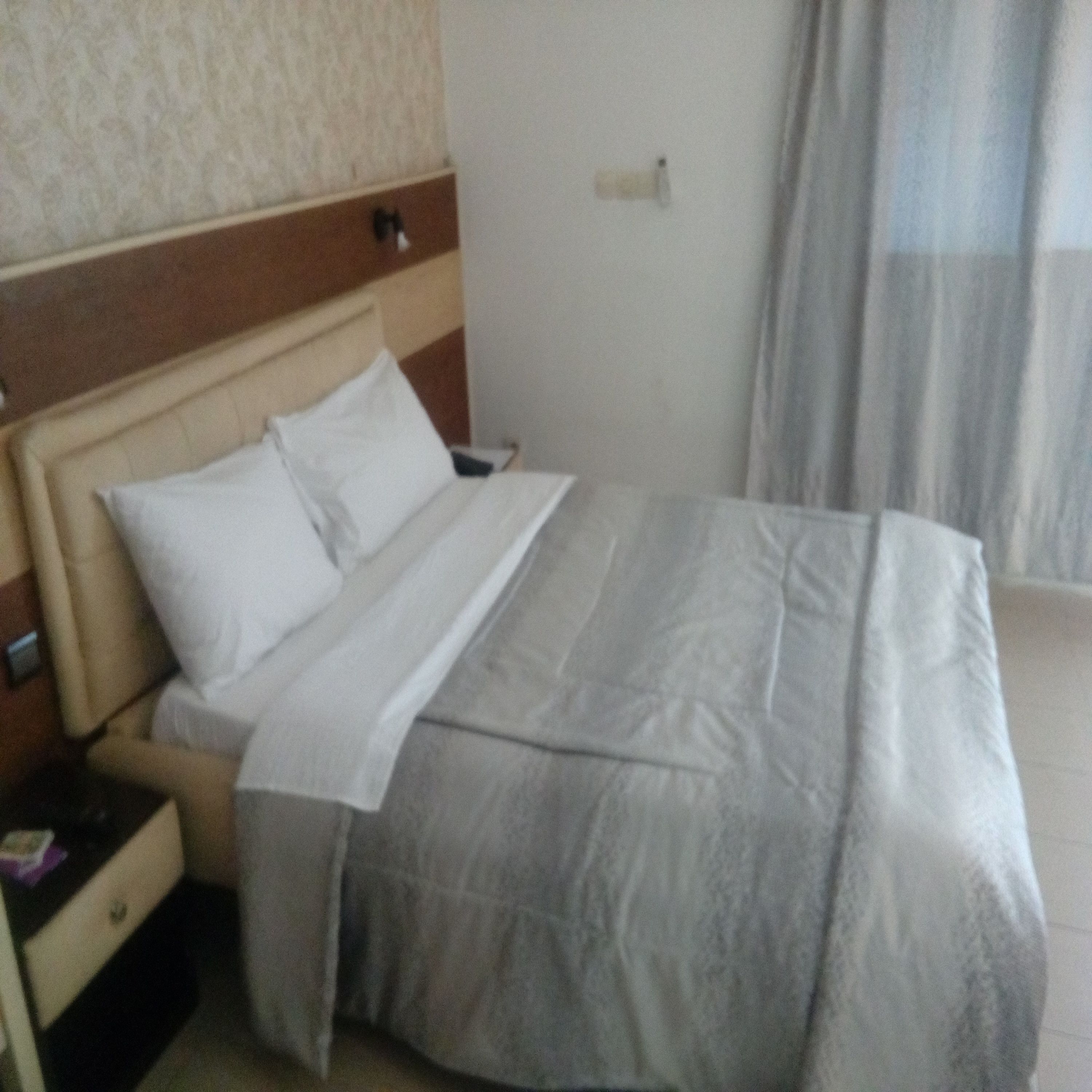 A hotel room with a bed, a nightstand, and a wall-mounted light.