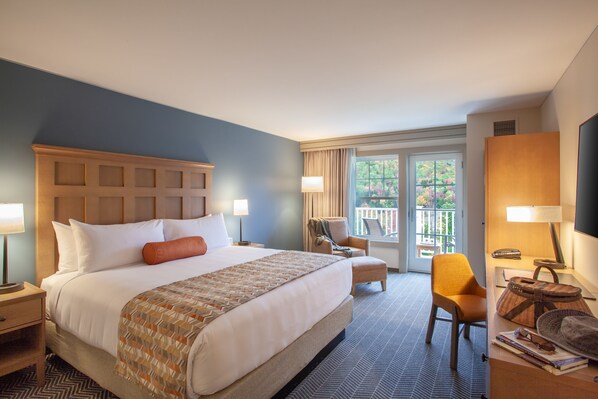 Habitación de hotel con una cama grande, una silla, un escritorio con lámpara y vistas al exterior.