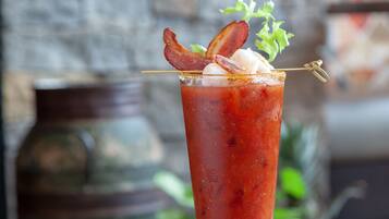 Un vaso alto de Bloody Mary con tocino y un ramito de apio sobre un posavasos de madera.