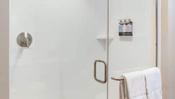 Doccia vetrata con porta in vetro, asciugamano e articoli da toilette.