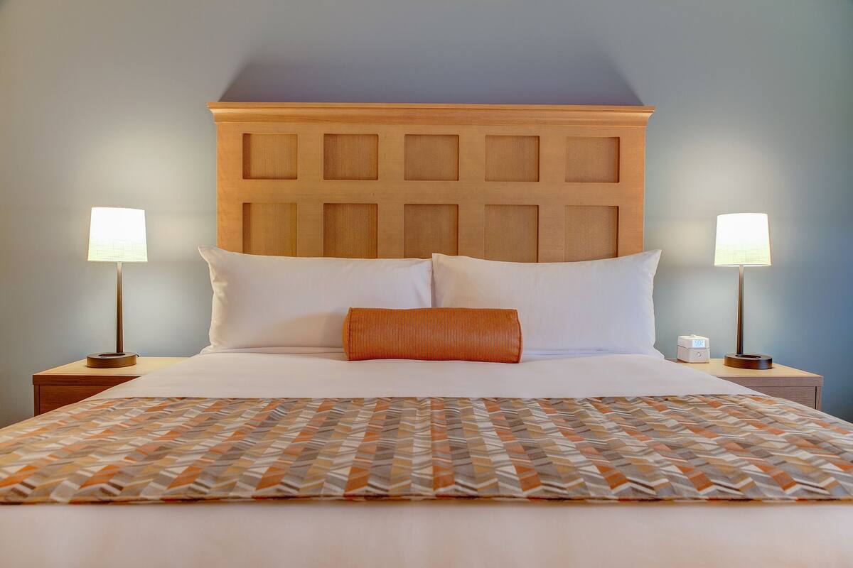 A neatly made bed with a patterned bedspread, two bedside lamps, and a wooden headboard.