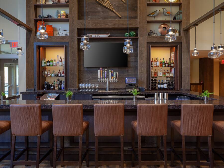 A bar area with a long counter, multiple bar stools, and a television mounted on the wall.