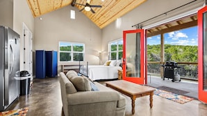 A modern interior with a wooden ceiling, a sofa, a table, a bed, and a balcony with a grill. - Hill Country Casitas (Dripping Springs)