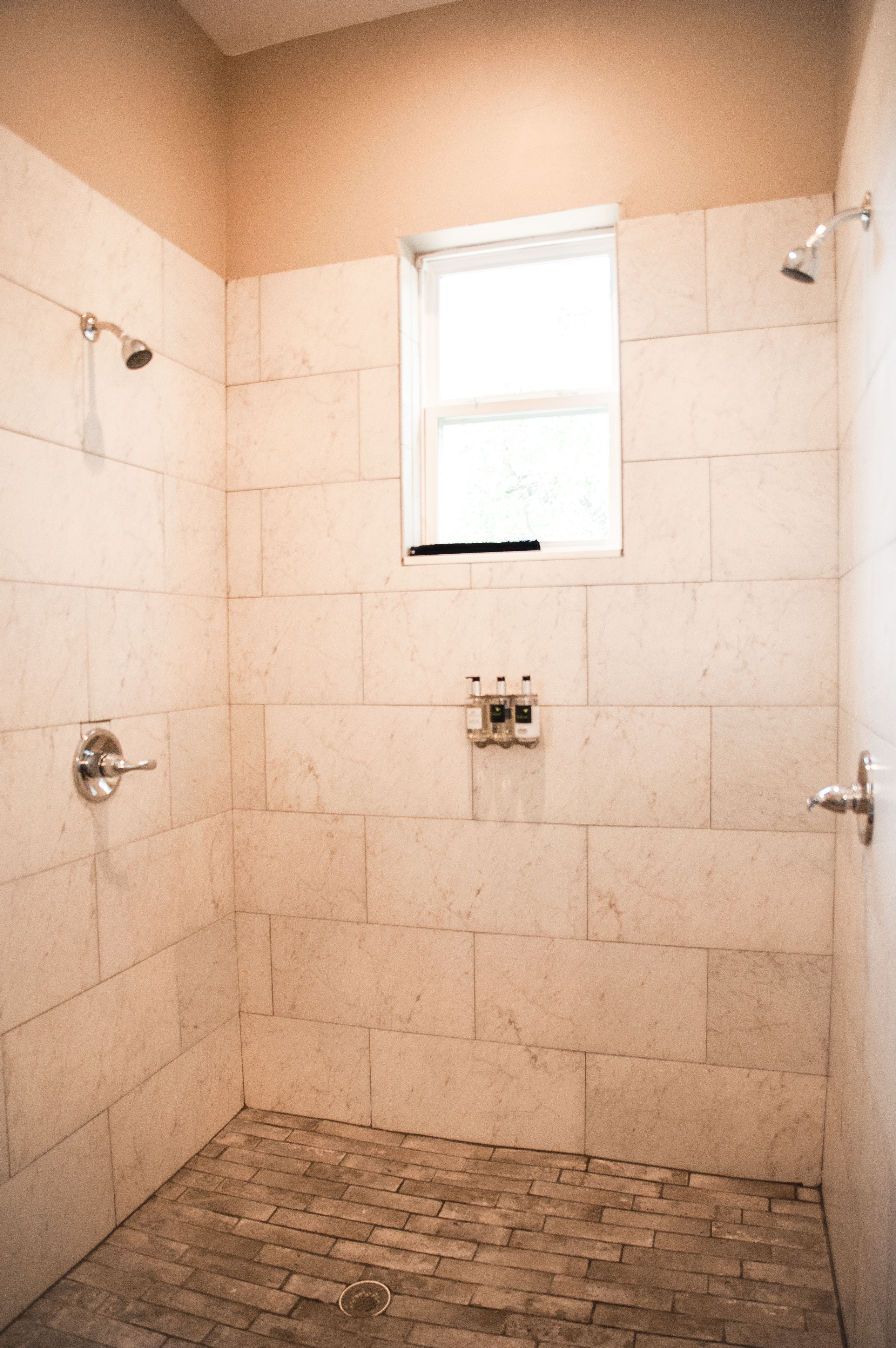 A small, enclosed shower area with a window, tiled walls, and a brick floor.