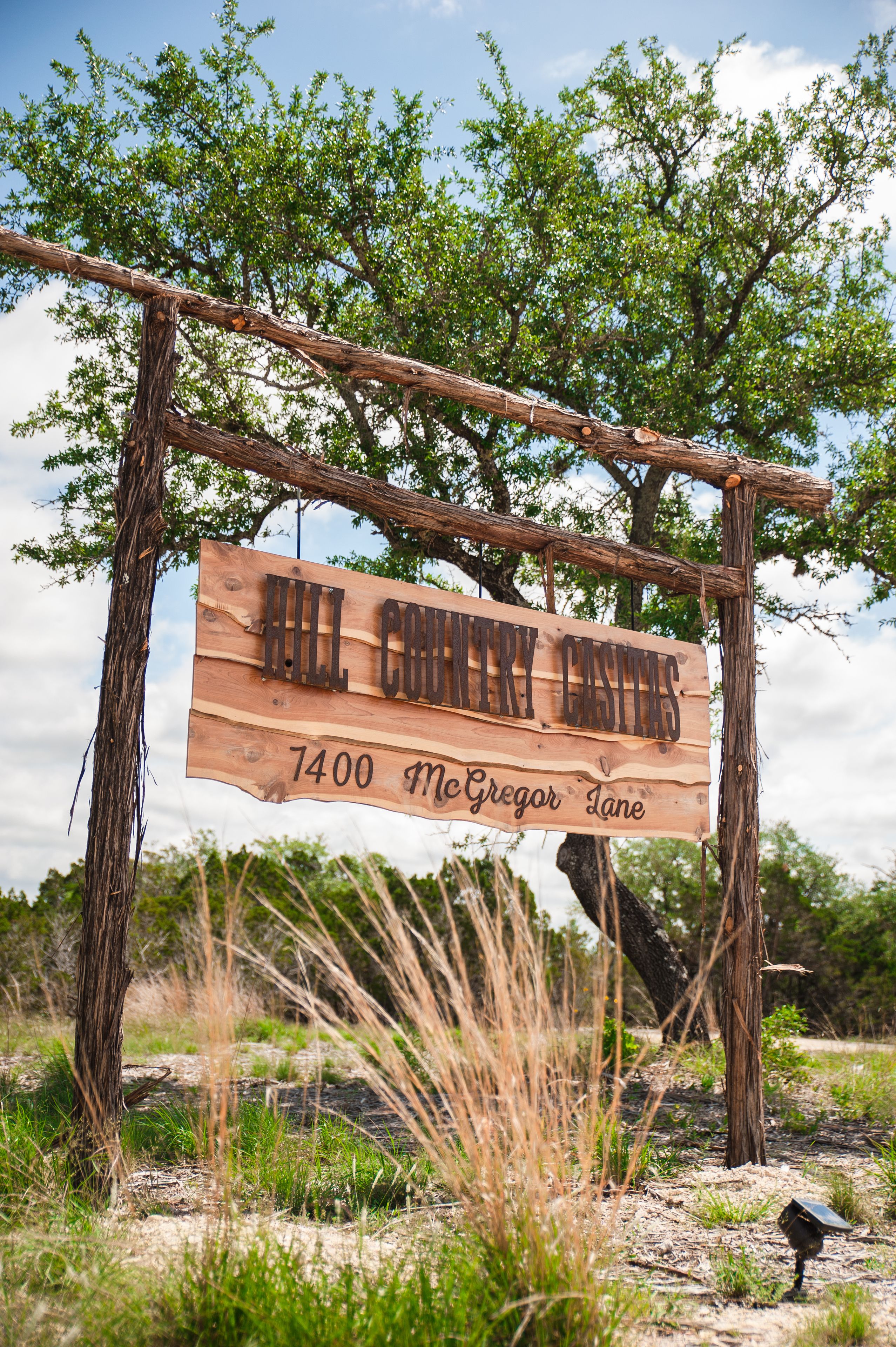 A wooden sign with the text "Hill County Estates 1400 McGregor Lane" in a rural setting.