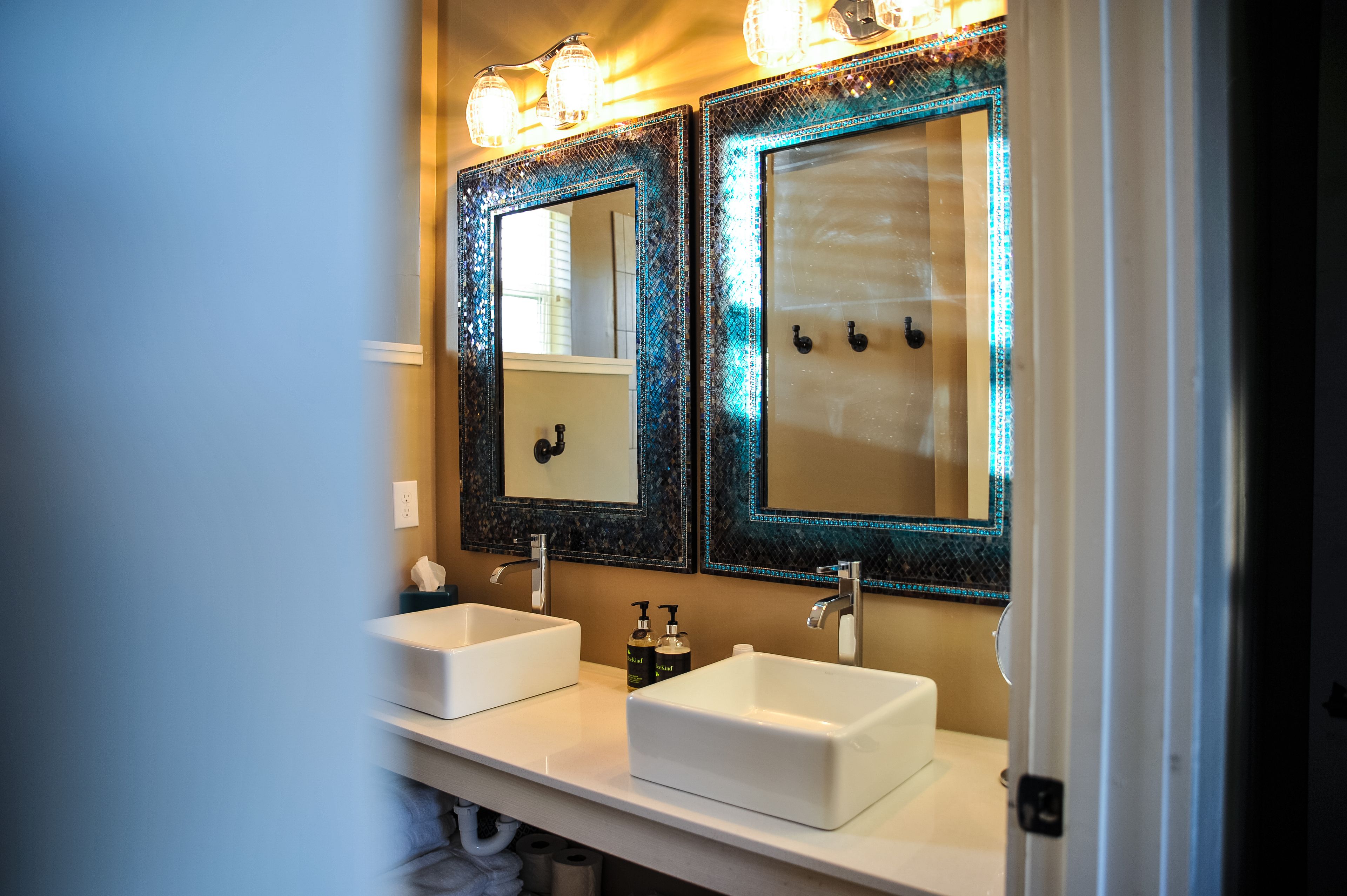 A bathroom with two white sinks, a mirror with decorative lights, and a towel rack.