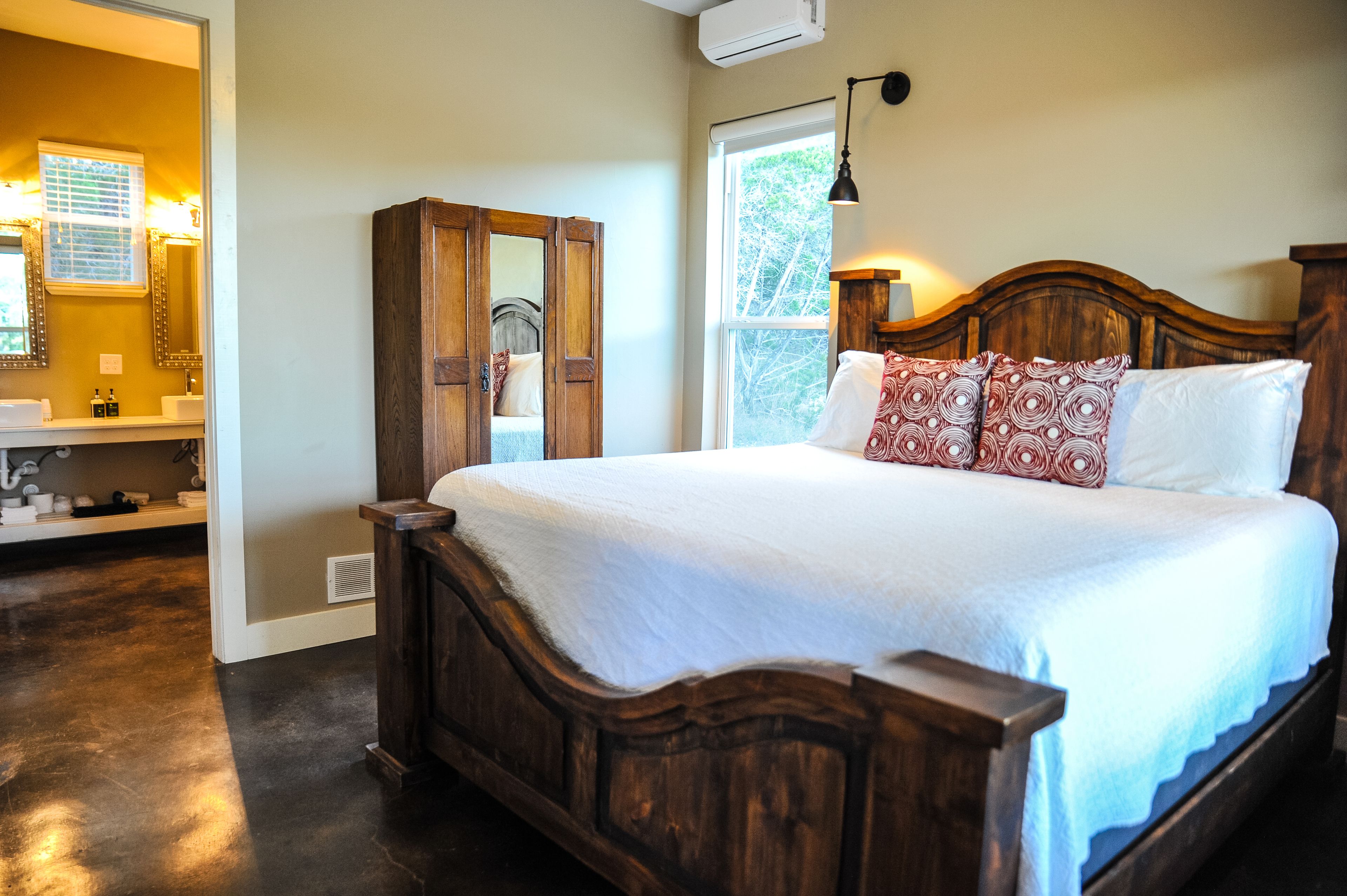 A bedroom with a wooden bed, a nightstand, a mirror, and a window with a view of trees.