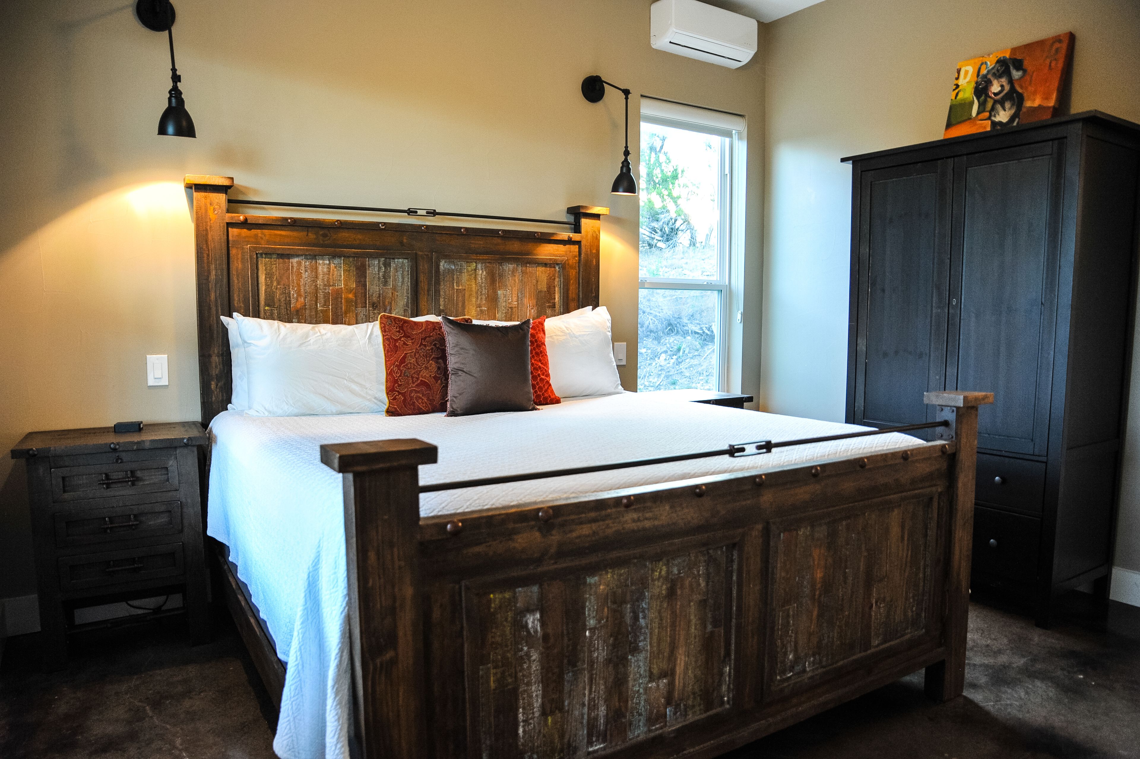 A wooden bed with white and red pillows, a nightstand, a wardrobe, and a window with natural light.