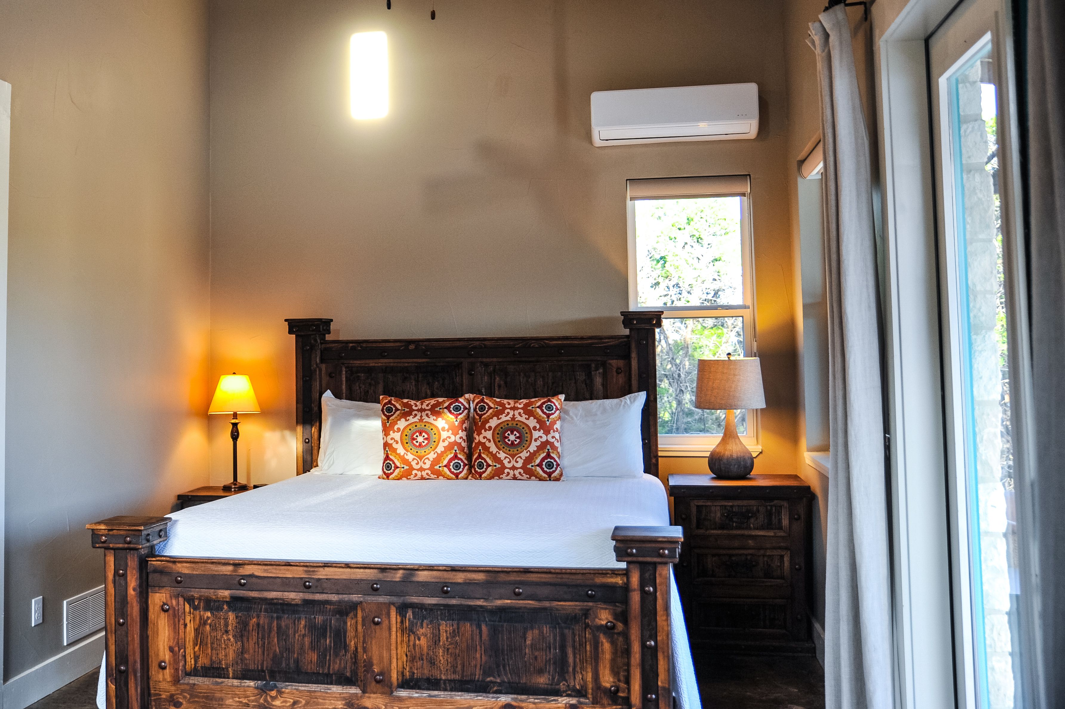 A wooden bed with patterned pillows, a bedside lamp, and a window with curtains.