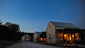 A stone building with a metal roof, a driveway, and a lit interior. - Hill Country Casitas (Dripping Springs)
