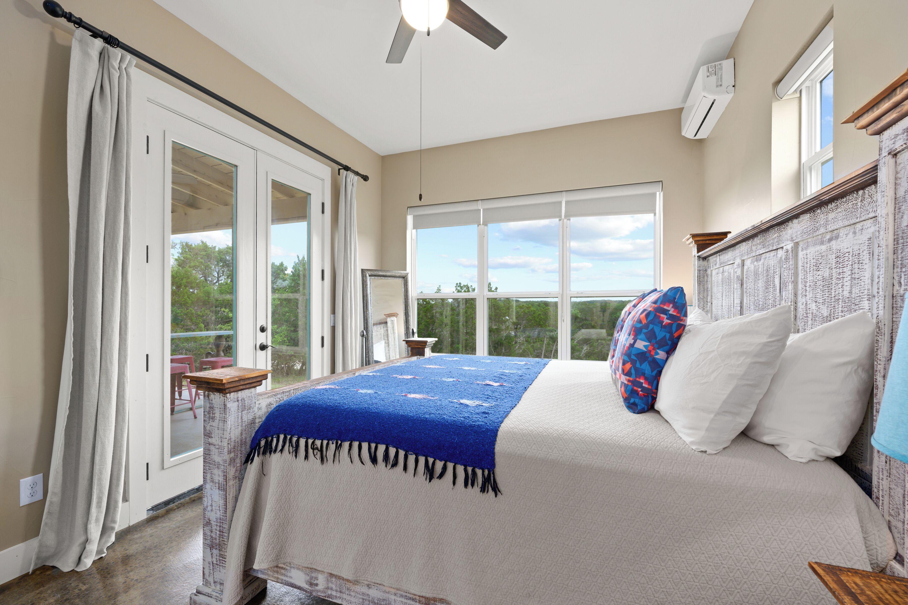 A bedroom with a large bed, a ceiling fan, a window with a view, and a sliding glass door leading to an outdoor area.