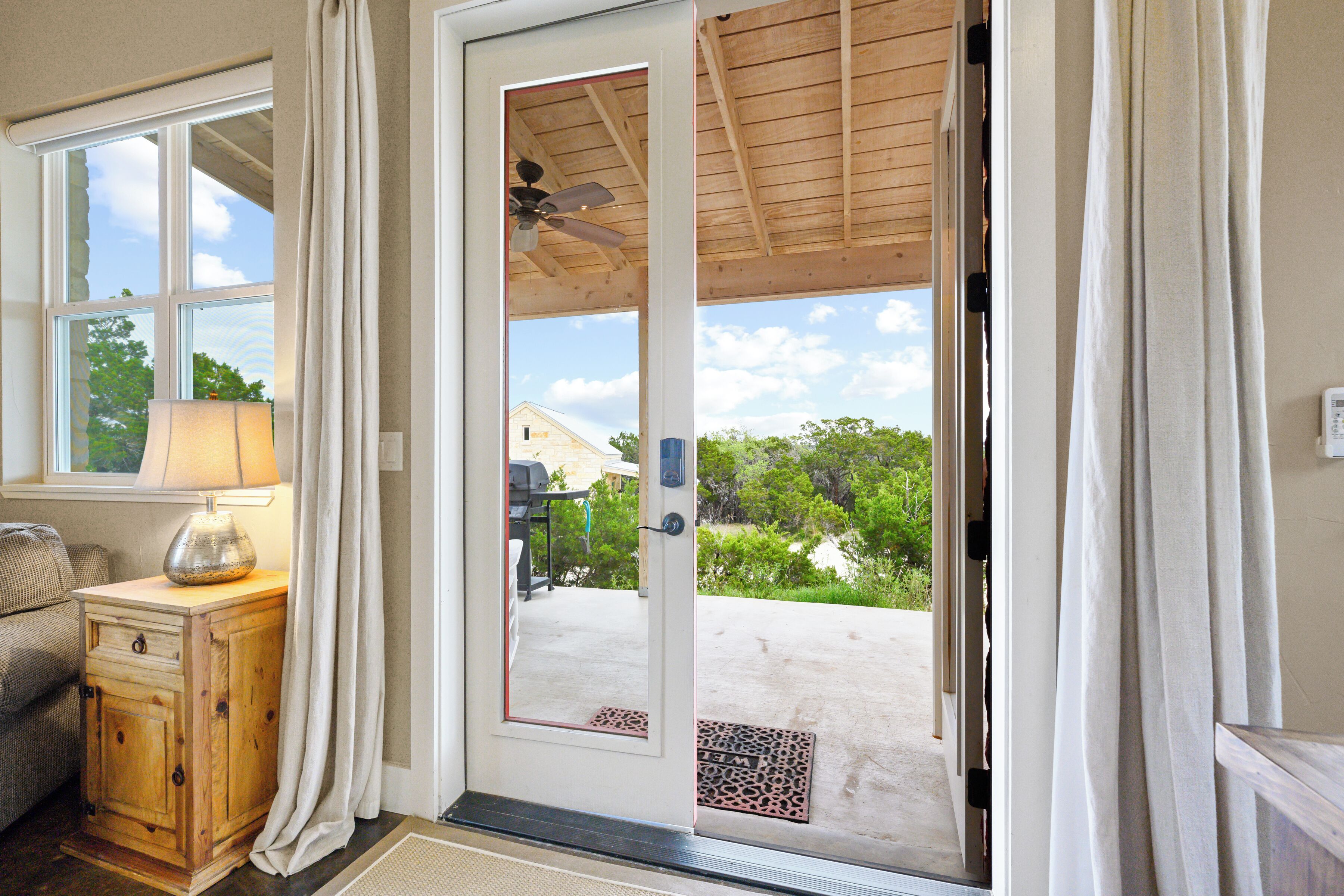 A room with a wooden cabinet, a lamp, and a sliding glass door leading to a patio with a ceiling fan and outdoor furniture.