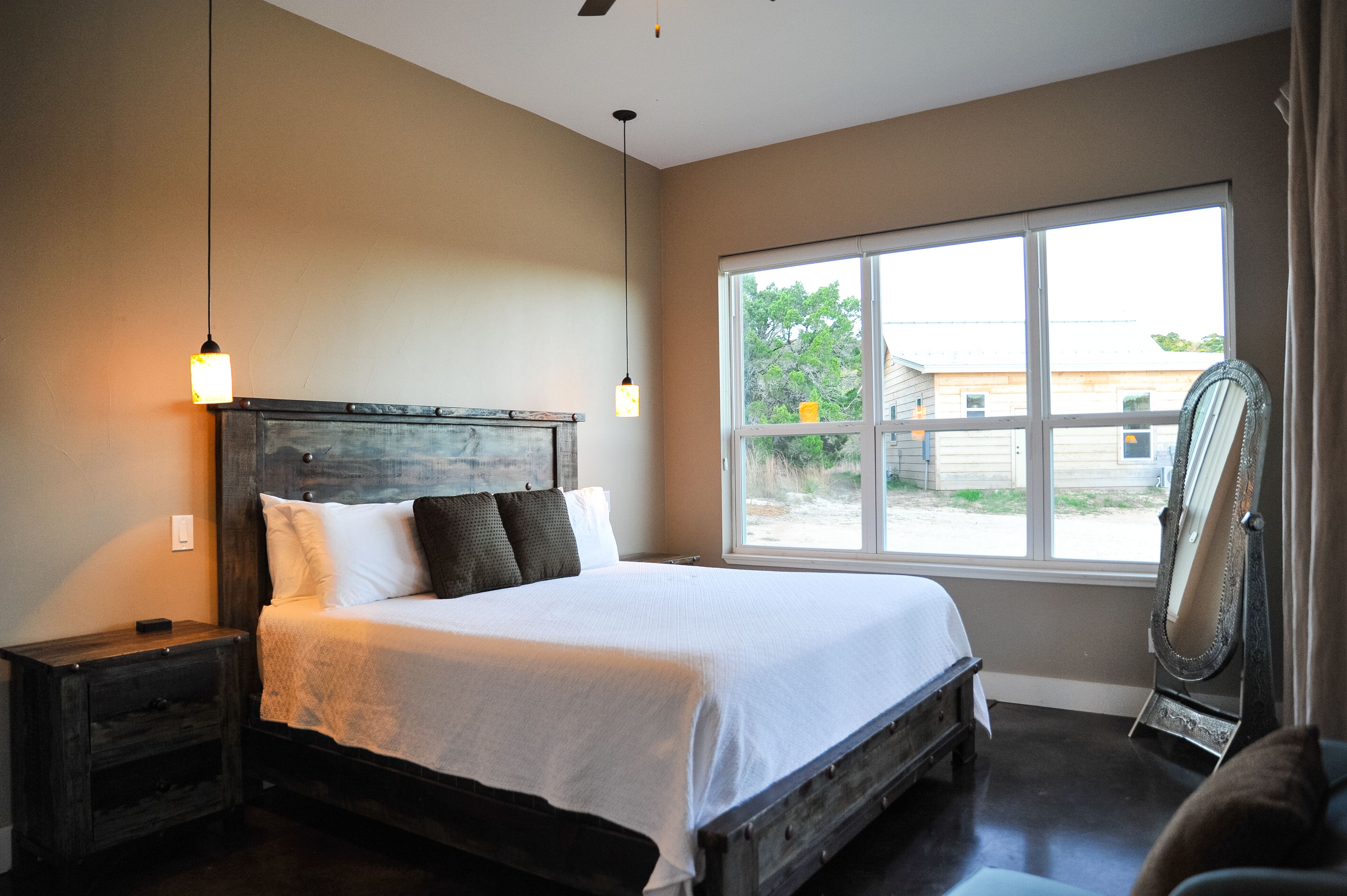 A bedroom with a large bed, a nightstand, a mirror, and a window with a view of the outside.