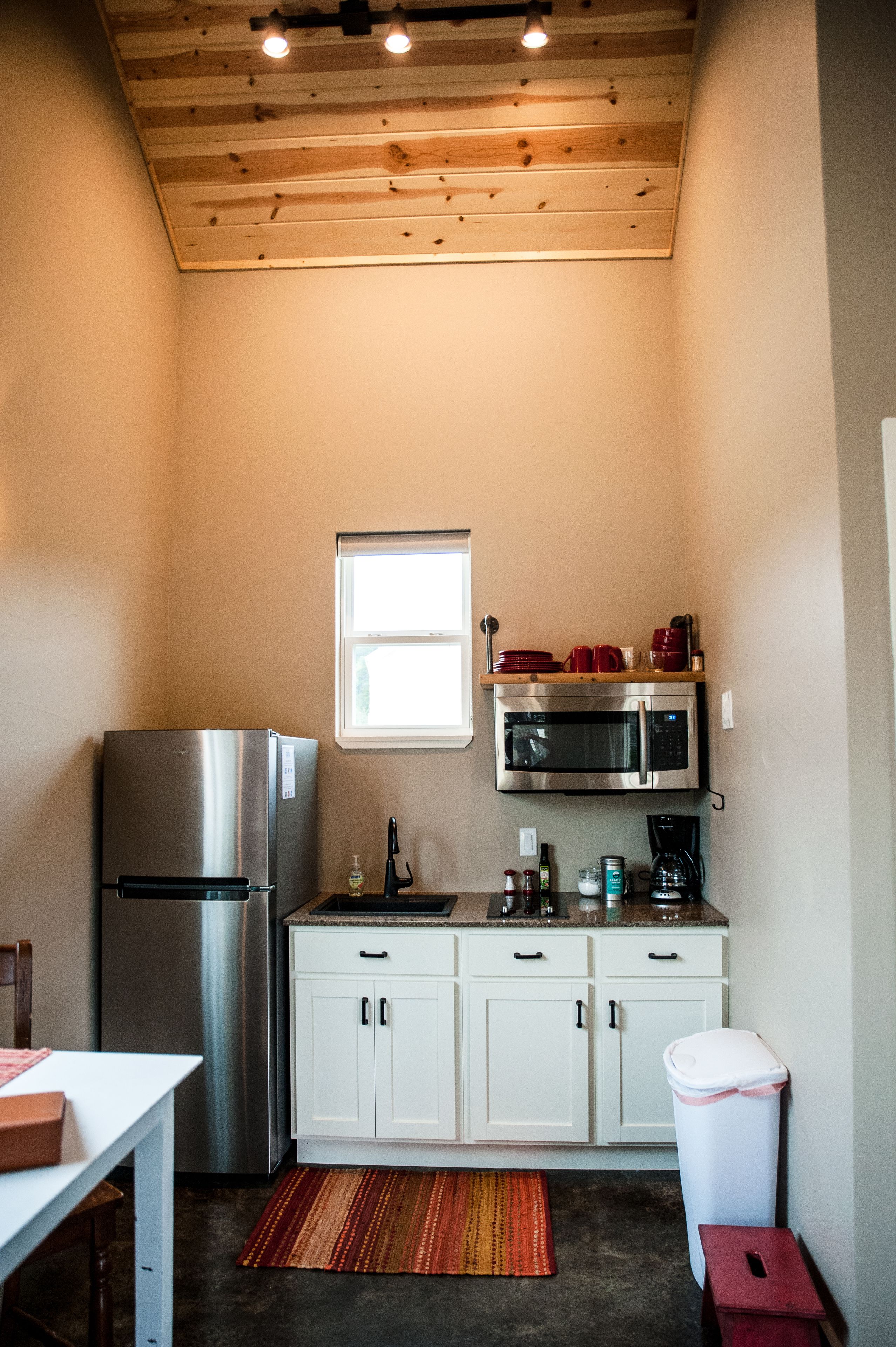 Una cocina compacta con un refrigerador de acero inoxidable, un microondas, gabinetes blancos y un ventanal pequeño.