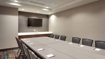 A conference room with a long table, chairs, a flat-screen TV, and a ceiling with recessed lighting.