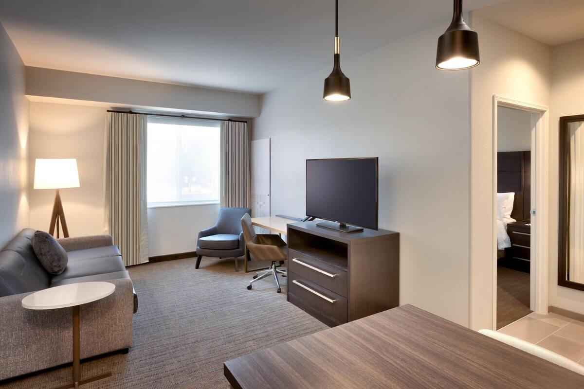 Ein modernes Hotelzimmer mit einer Couch, einem Schreibtisch, einem Fernseher und einem Esstisch.